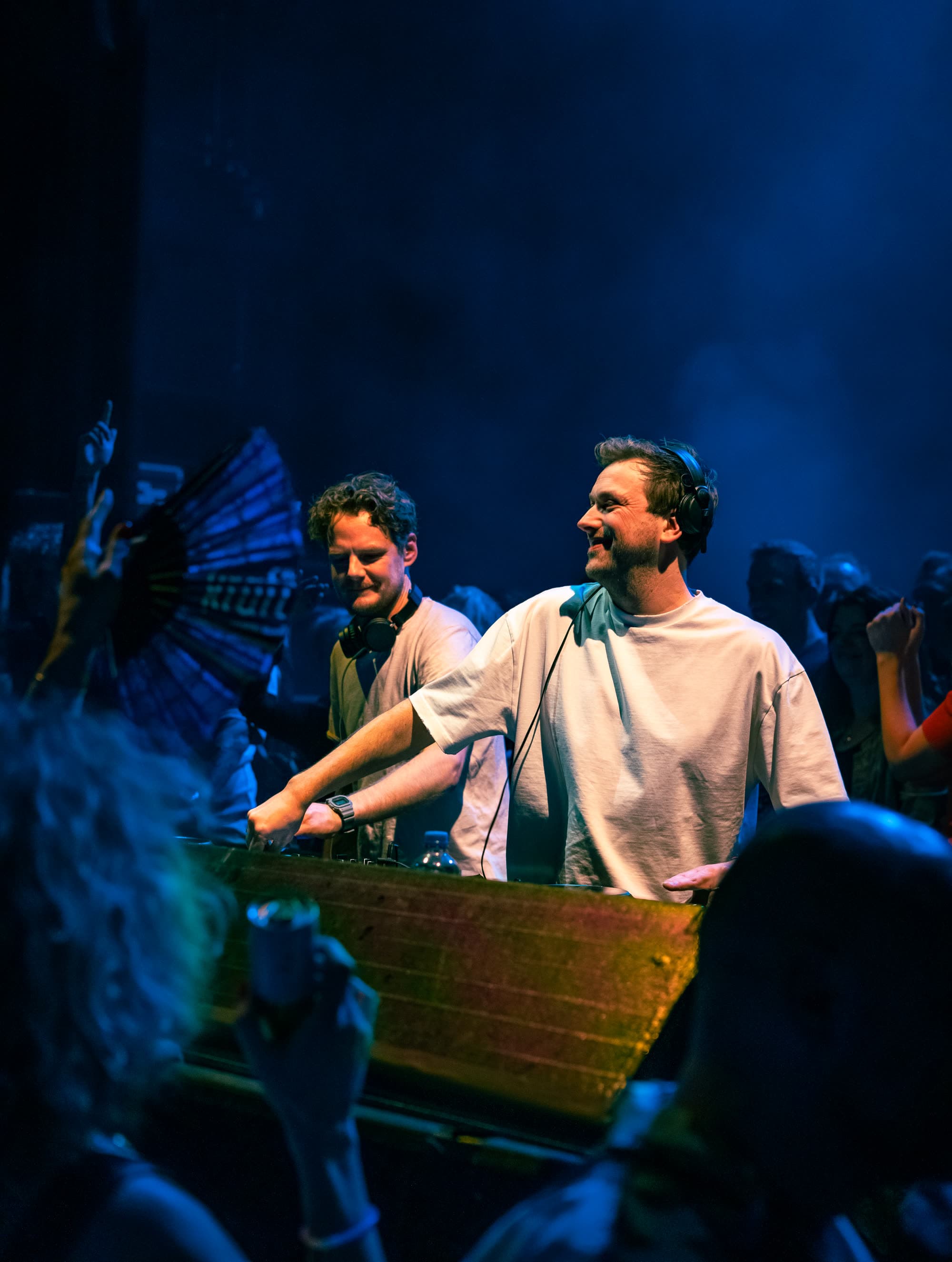 Twee dj's lachen achter de draaitafels in blauw licht