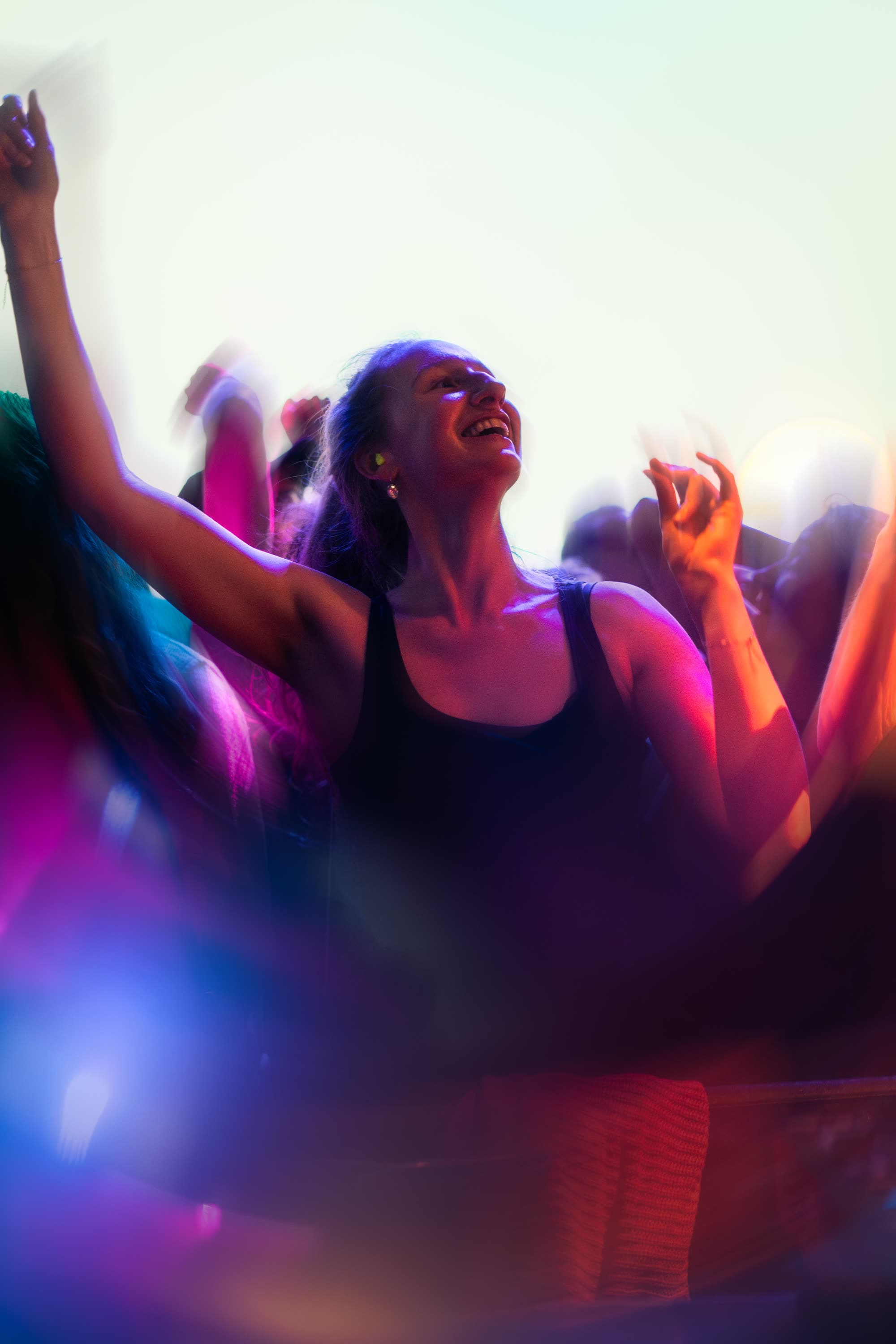 Lachende bezoeker danst met haar arm in de lucht in roze licht