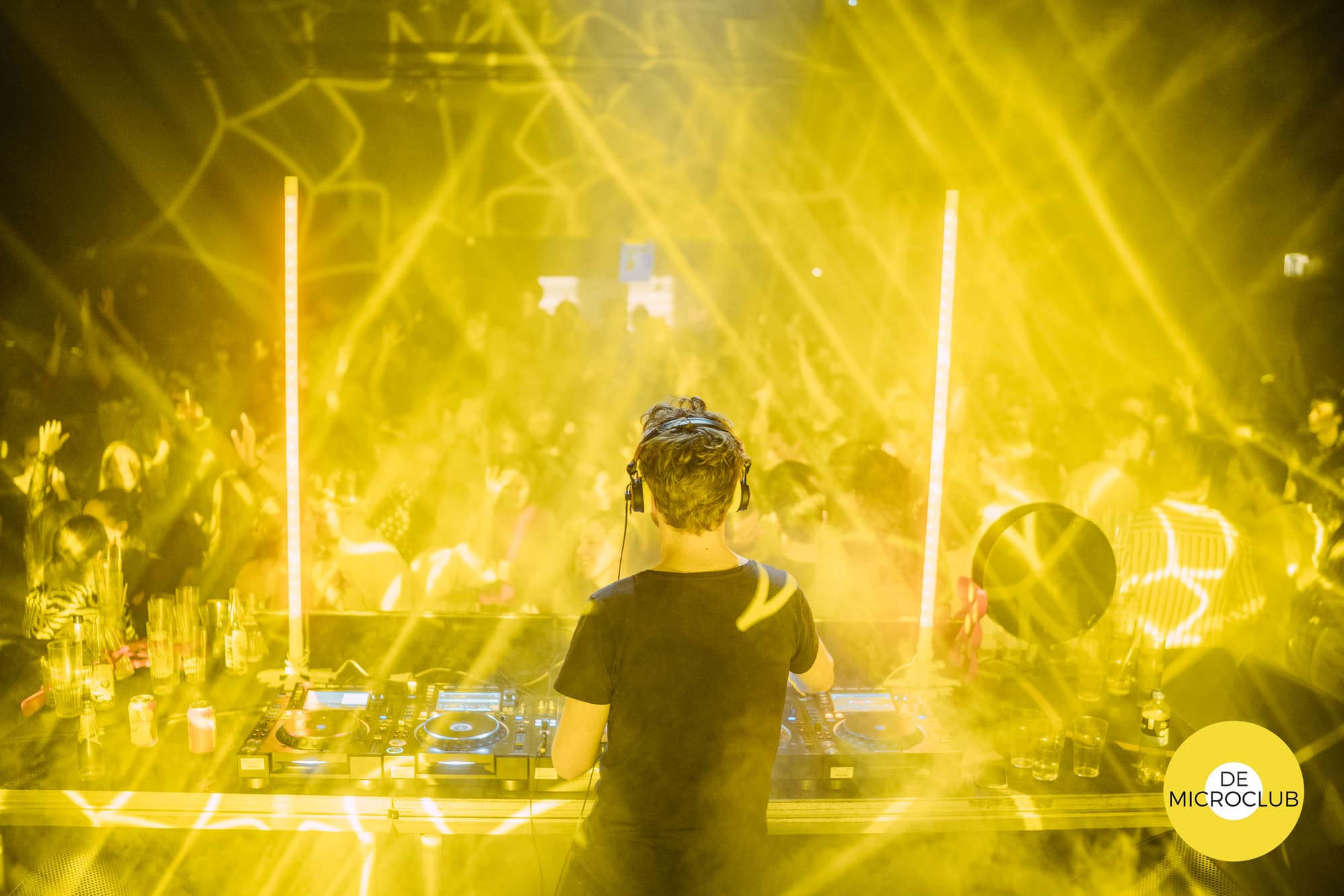 DJ achter de draaitafels met gele lasers over de volle dansvloer