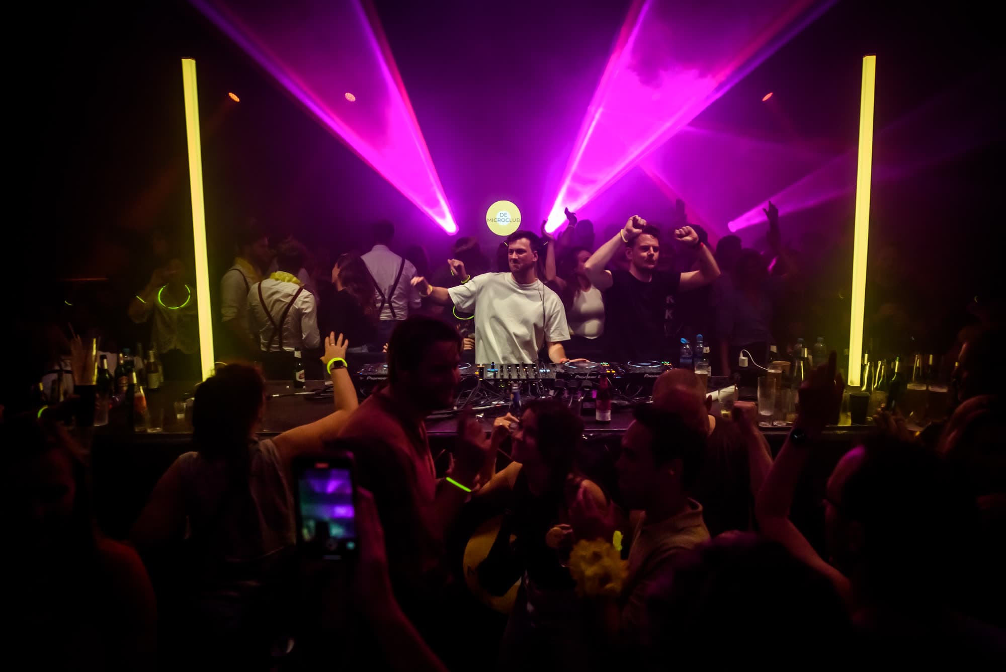 Roze lichtbundels boven de DJ-booth en het dansende publiek