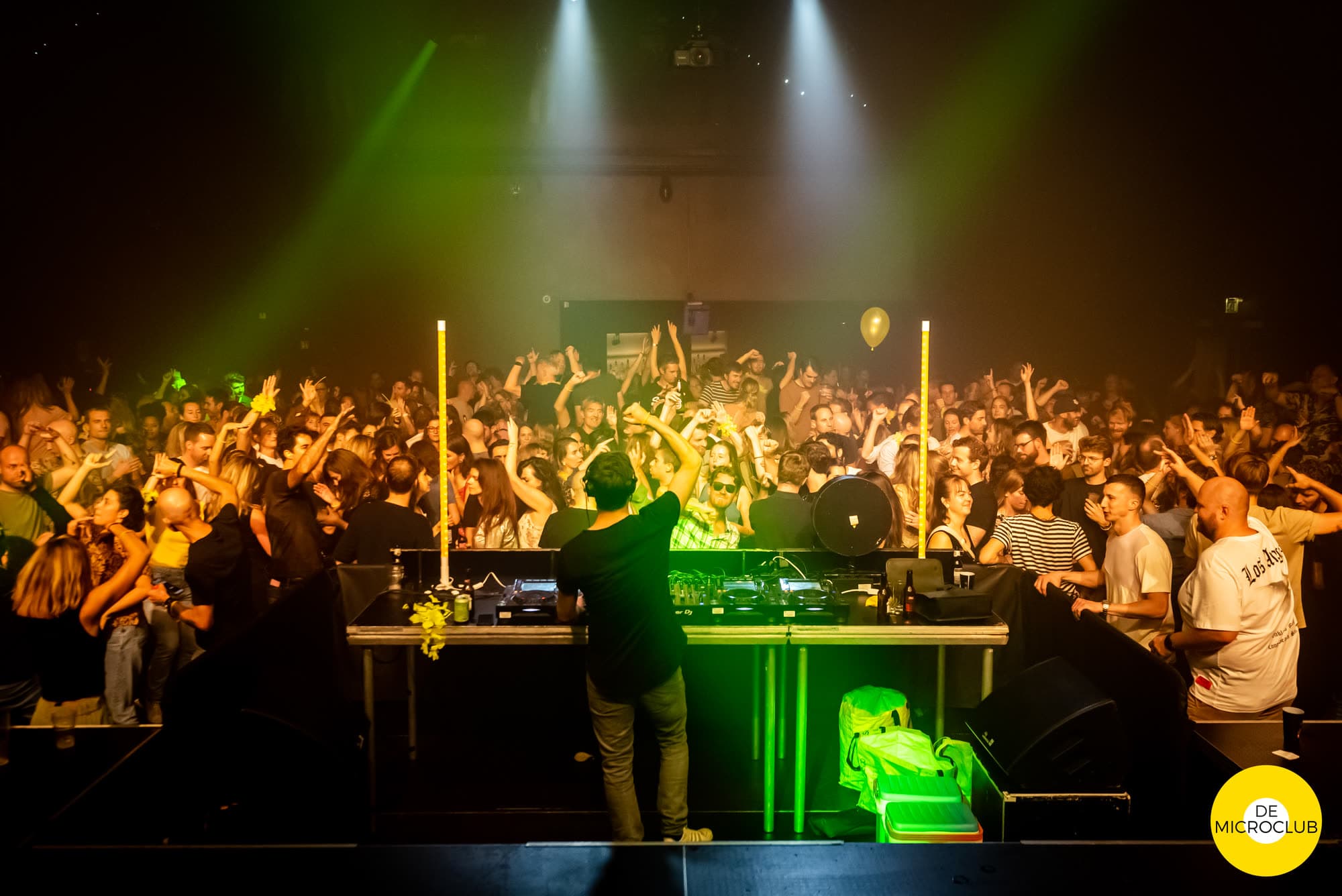 DJ met zijn rug naar de camera voor een volle zaal in groen licht